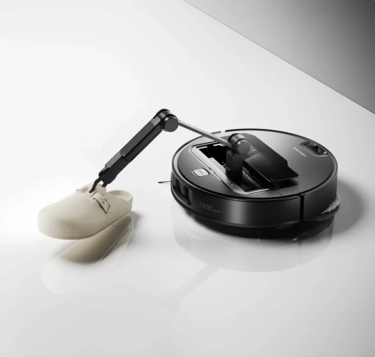 Un aspirateur robot noir roborock z70 avec un bras robotisé qui tire sur une chaussure blanche.