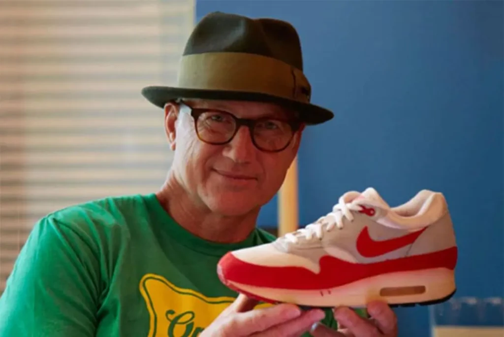 Portrait de Tinker Hatfield, designer de Nike, tenant fièrement une chaussure Air Max 1 rouge et blanche.