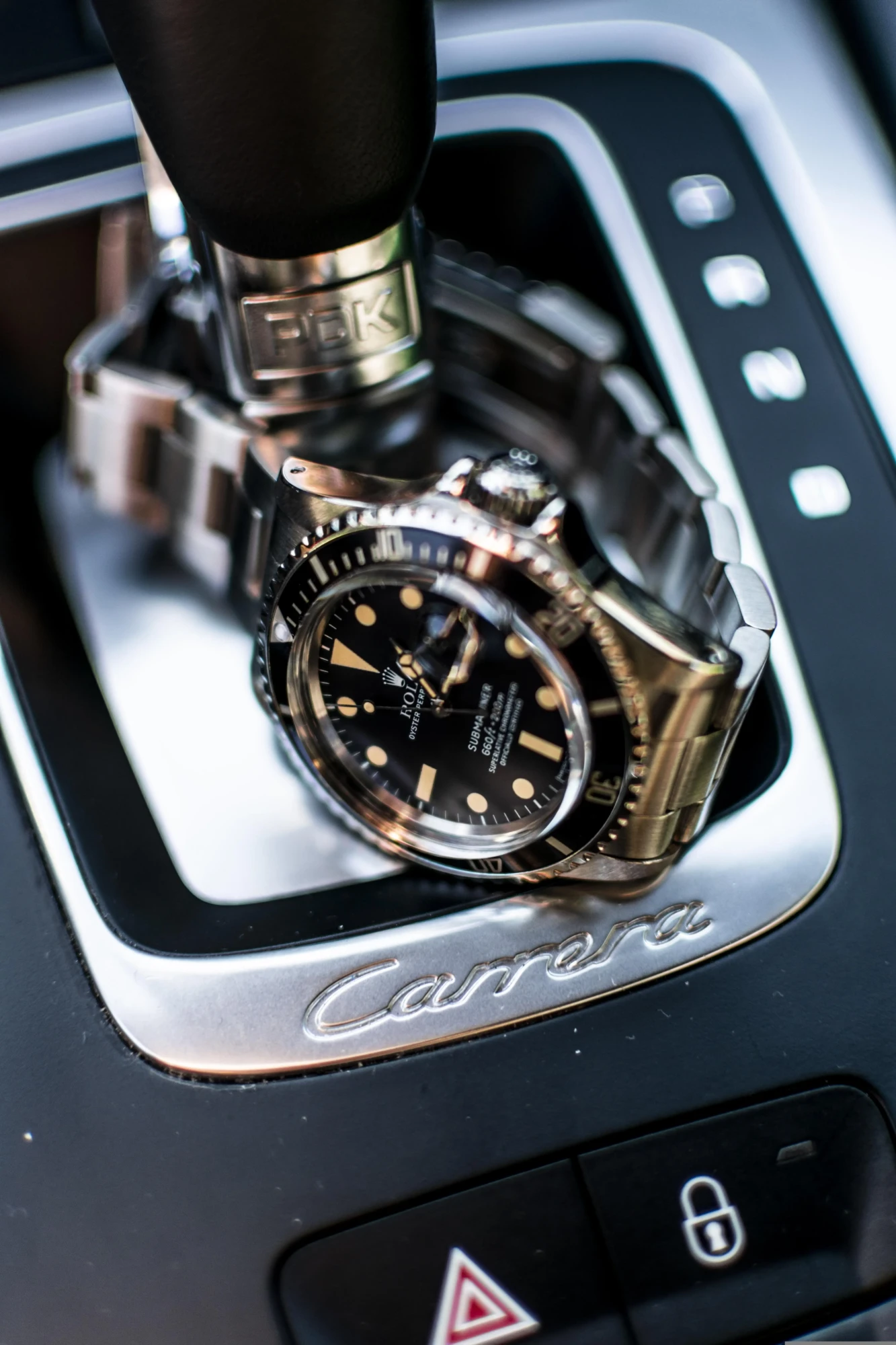 Une montre Rolex Submariner en acier inoxydable posée sur la console centrale et le levier de vitesse d'une voiture de sport Porsche Carrera.